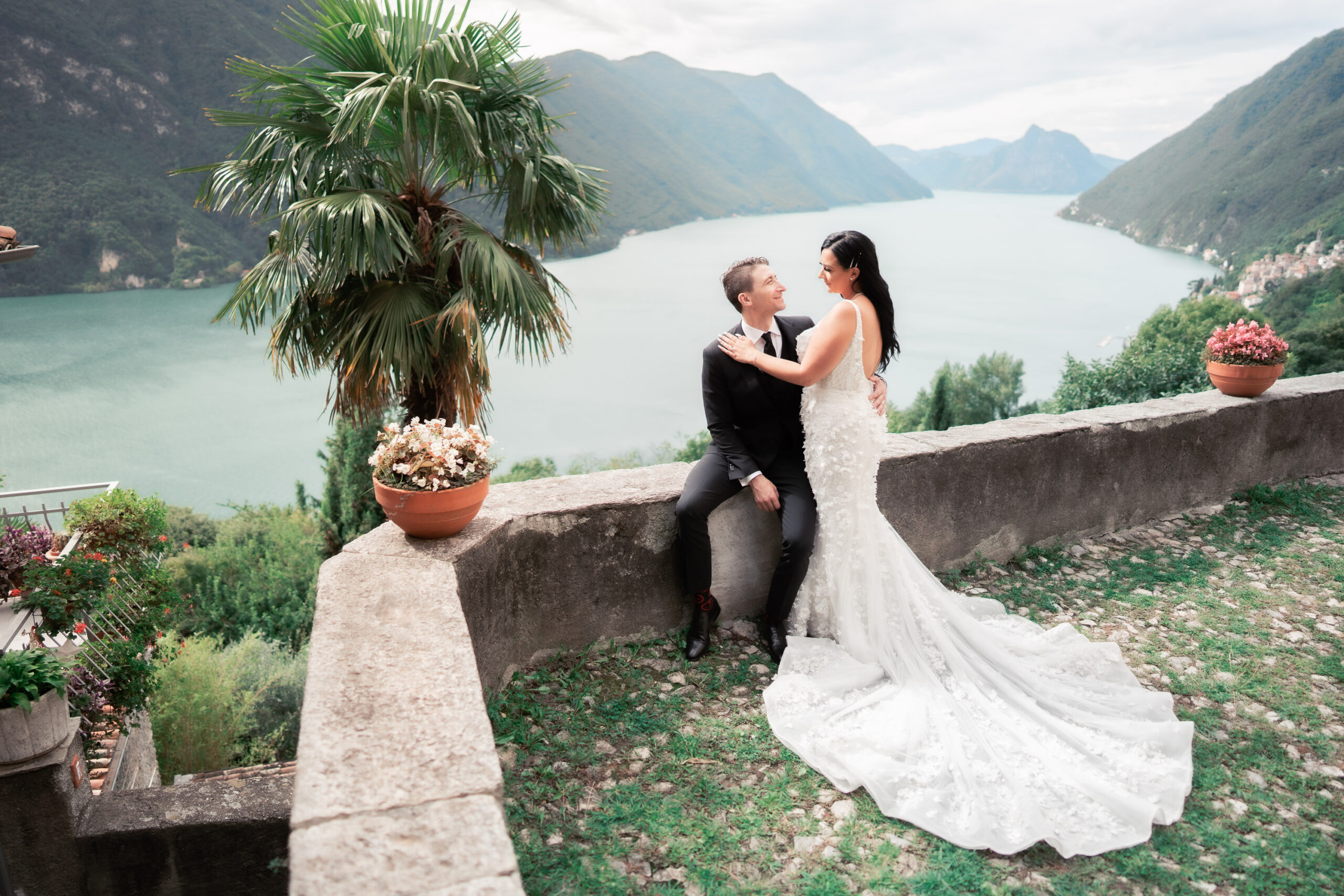 Bride and groom overlooking Lake Como during an intimate destination wedding, seated on a stone terrace with sweeping mountain views.